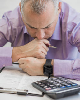 Feeling sick and tired. Frustrated young man keeping eyes closed while sitting at his working place in office